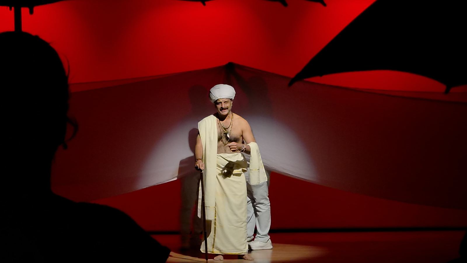 Actor in white costume under a tight spotlight against deep red light